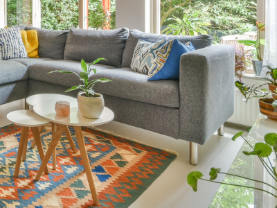 Luxury Outdoor Living A gray sectional sofa with patterned cushions sits next to a small white coffee table with plants, on a colorful geometric rug in a bright living room with large windows, blending indoor comfort with luxury outdoor living vibes. Toronto Contractors