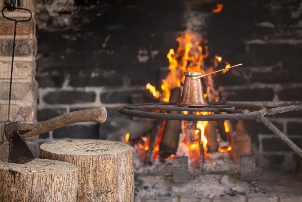 Luxury Outdoor Living A metal pot is heating over an open fire on a metal grate, with an axe resting on a tree stump in the foreground—capturing the essence of luxury outdoor living. Toronto Contractors