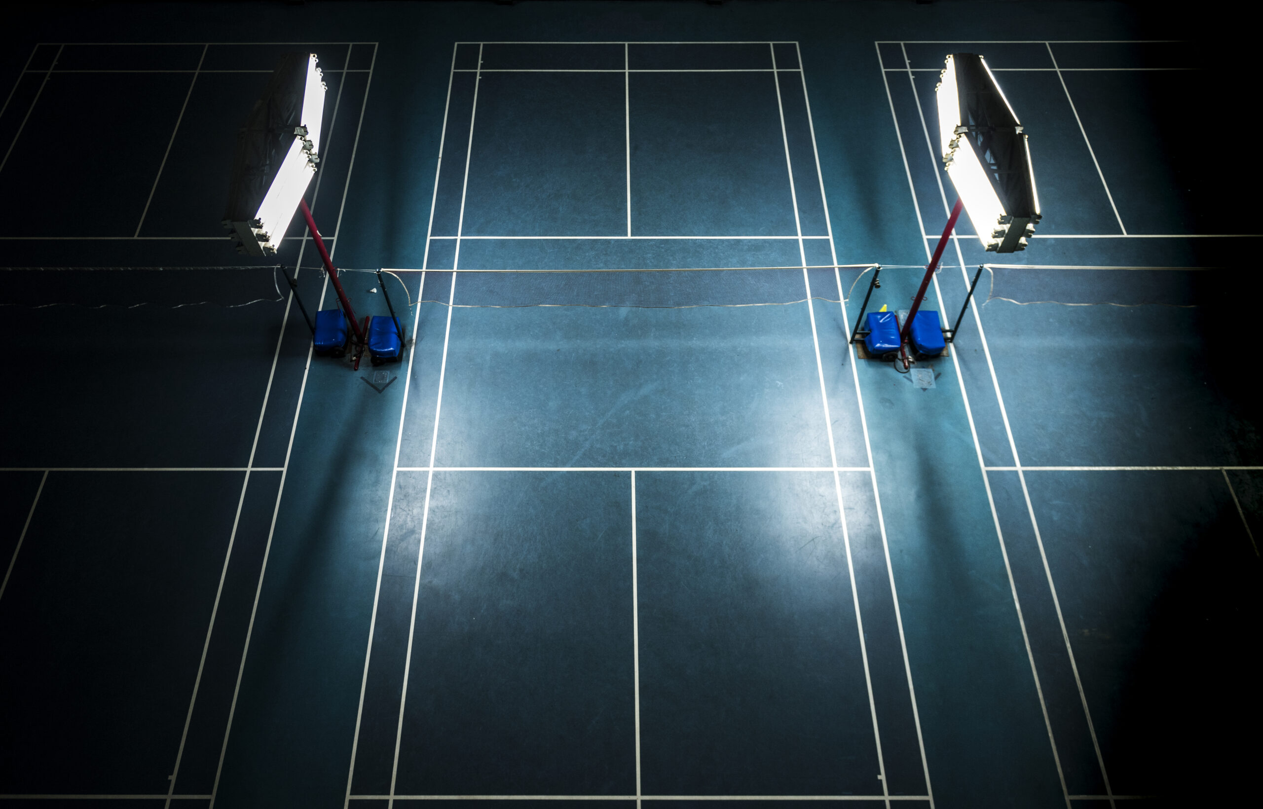 Luxury Outdoor Living Overhead view of two empty badminton courts under bright artificial lights on a dark blue floor, evoking the ambiance of luxury outdoor living. Toronto Contractors