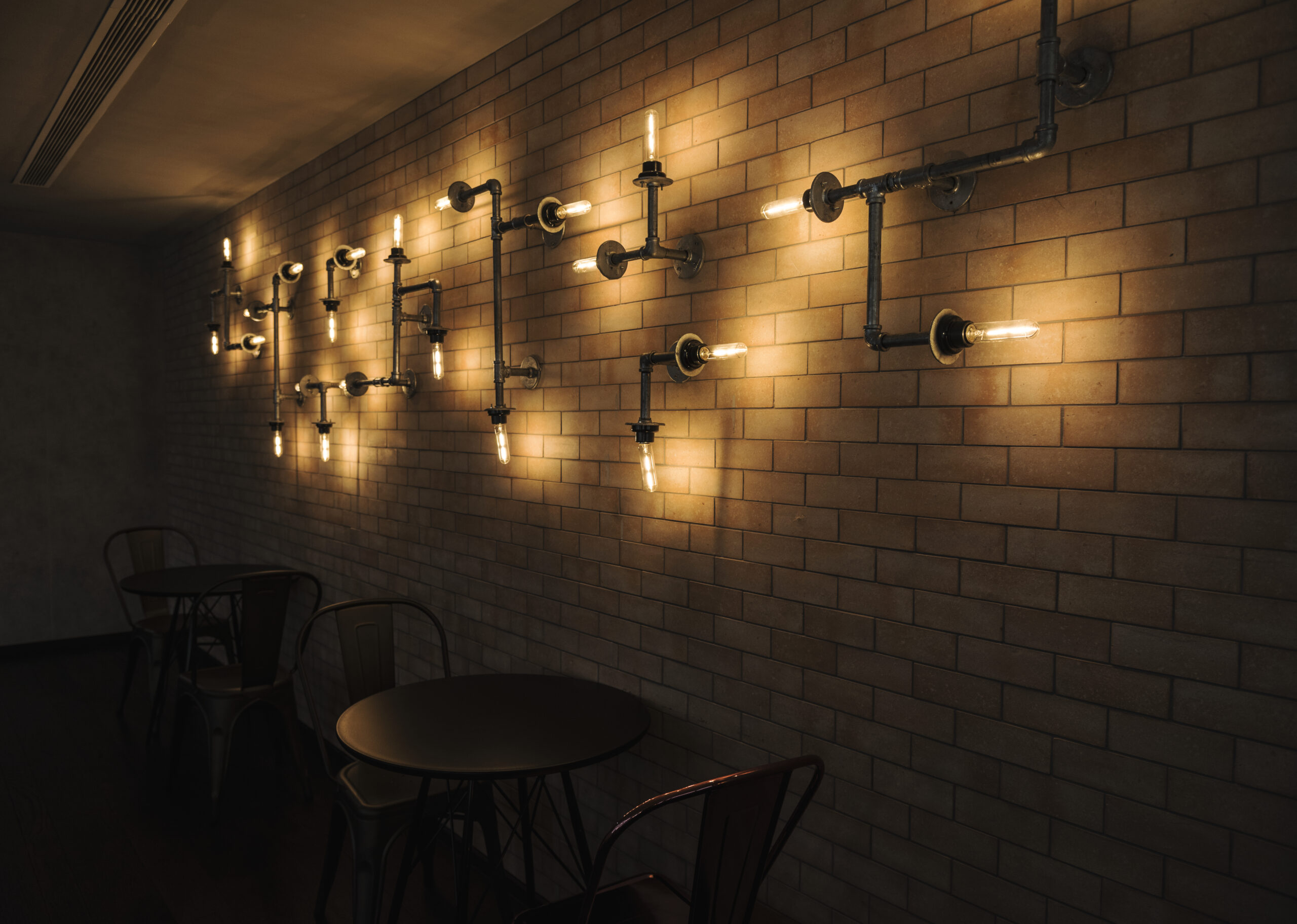 Luxury Outdoor Living Dimly lit cafe with industrial-style exposed pipe lighting fixed on a brick wall, and several round tables with chairs below—perfect for those who appreciate touches of luxury outdoor living in an urban setting. Toronto Contractors