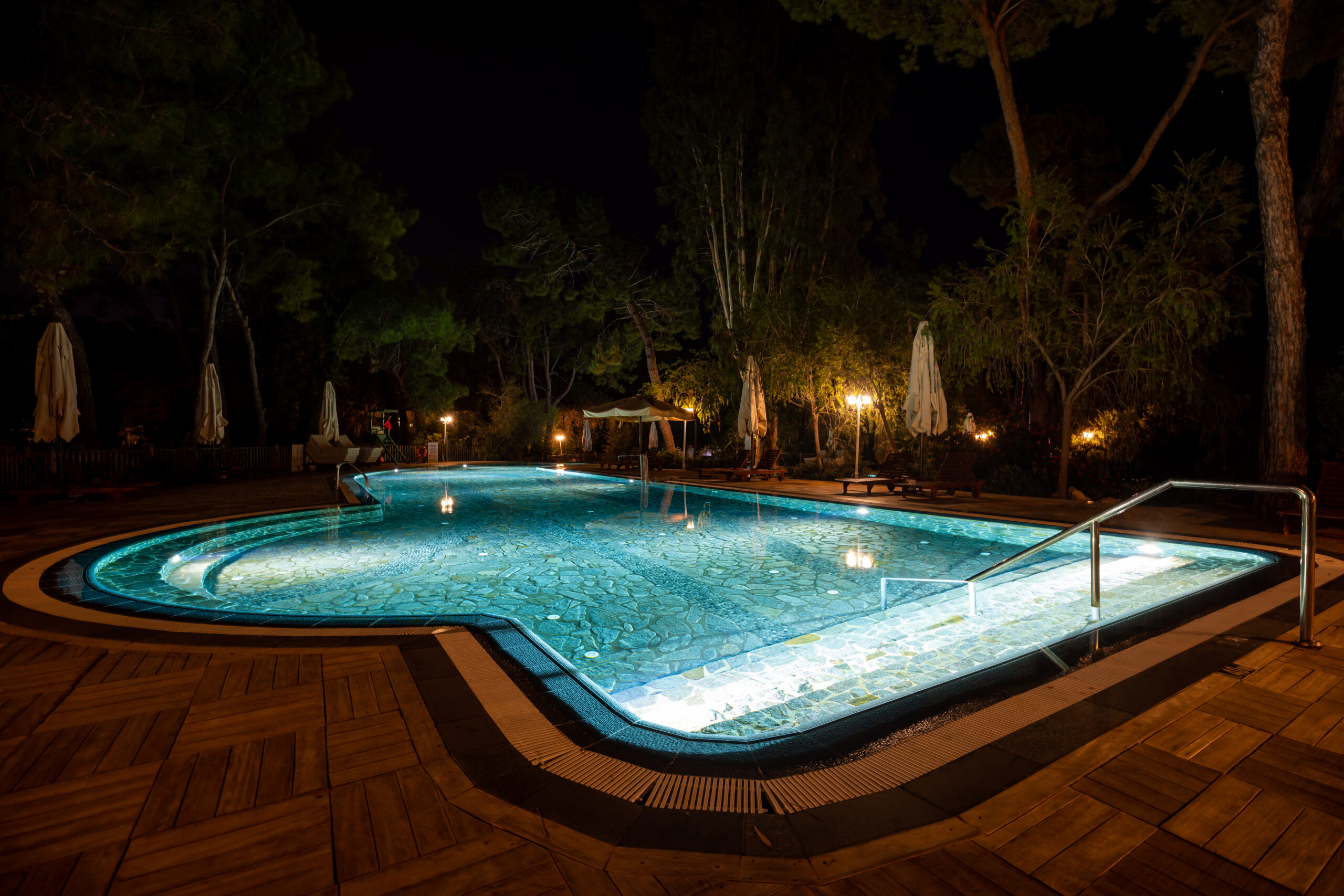 Luxury Outdoor Living Luxury Outdoor Living is showcased by this illuminated outdoor swimming pool at night, surrounded by trees and empty lounge chairs, with sleek metal handrails and closed umbrellas completing the serene scene. Toronto Contractors