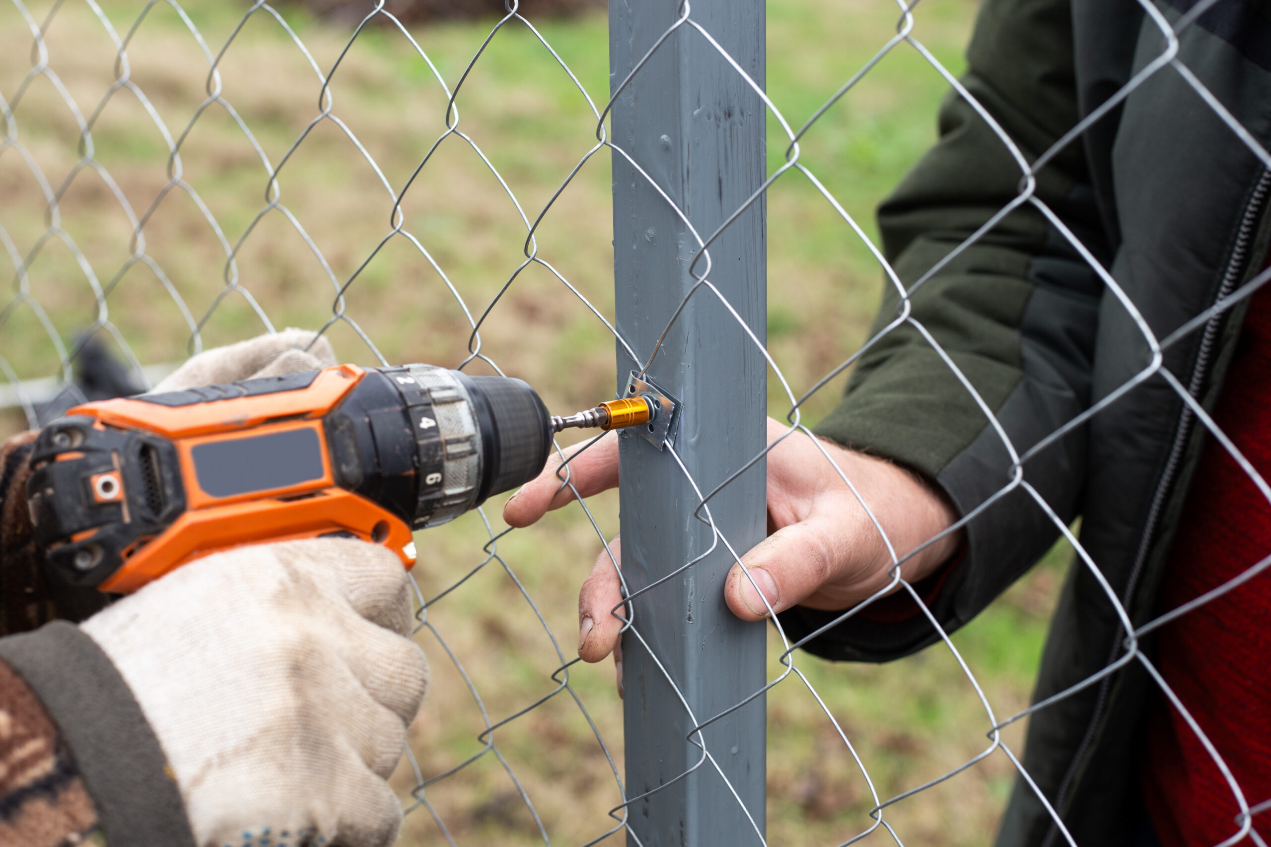 Luxury Outdoor Living A person uses a power drill to fasten a metal wire fence to a metal post, while another holds the post steady—building the foundation for luxury outdoor living. Toronto Contractors