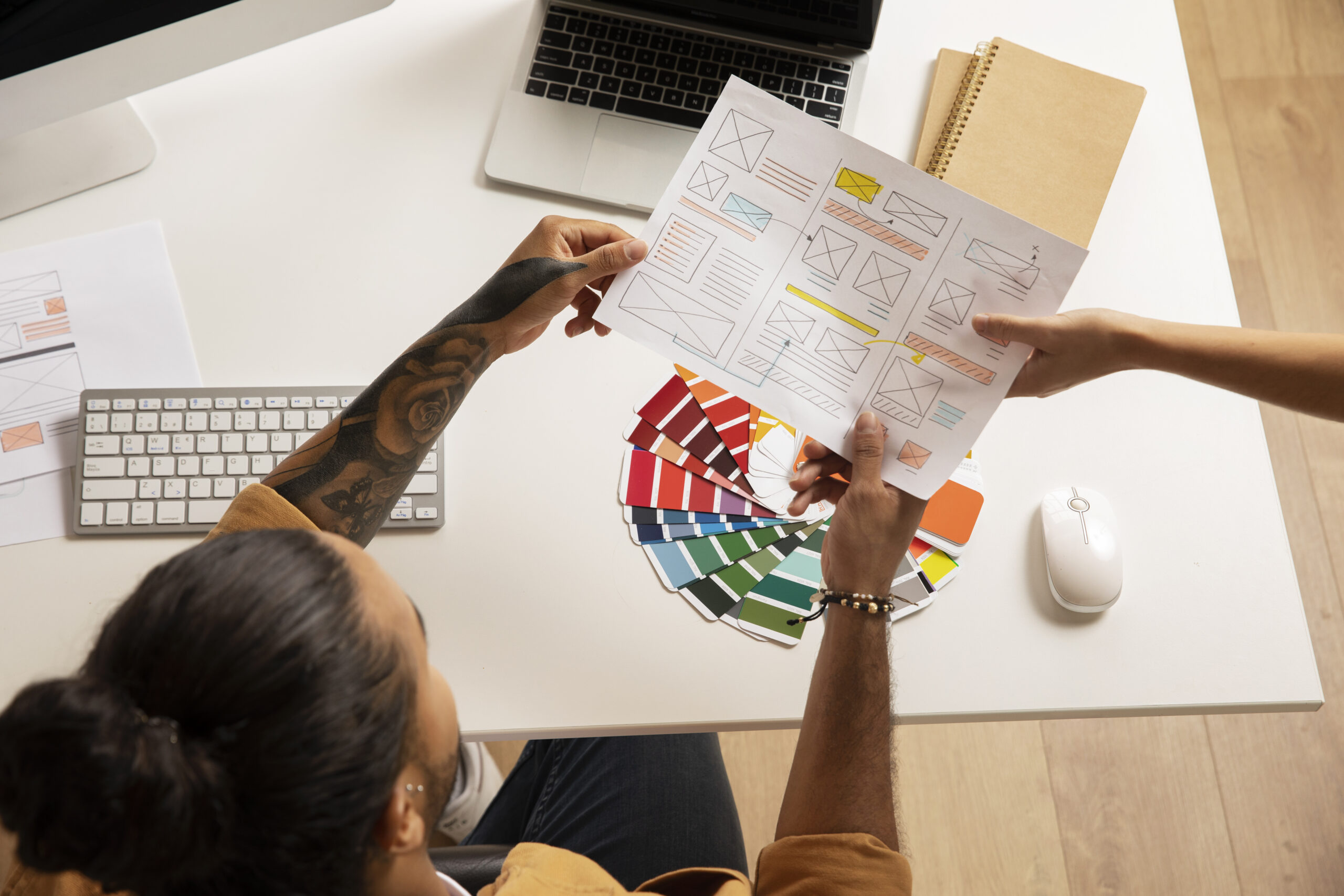 Luxury Outdoor Living Two people review a website wireframe printout and color palette samples at a desk, designing for a Luxury Outdoor Living brand, surrounded by a keyboard, mouse, laptop, and notebook. Toronto Contractors