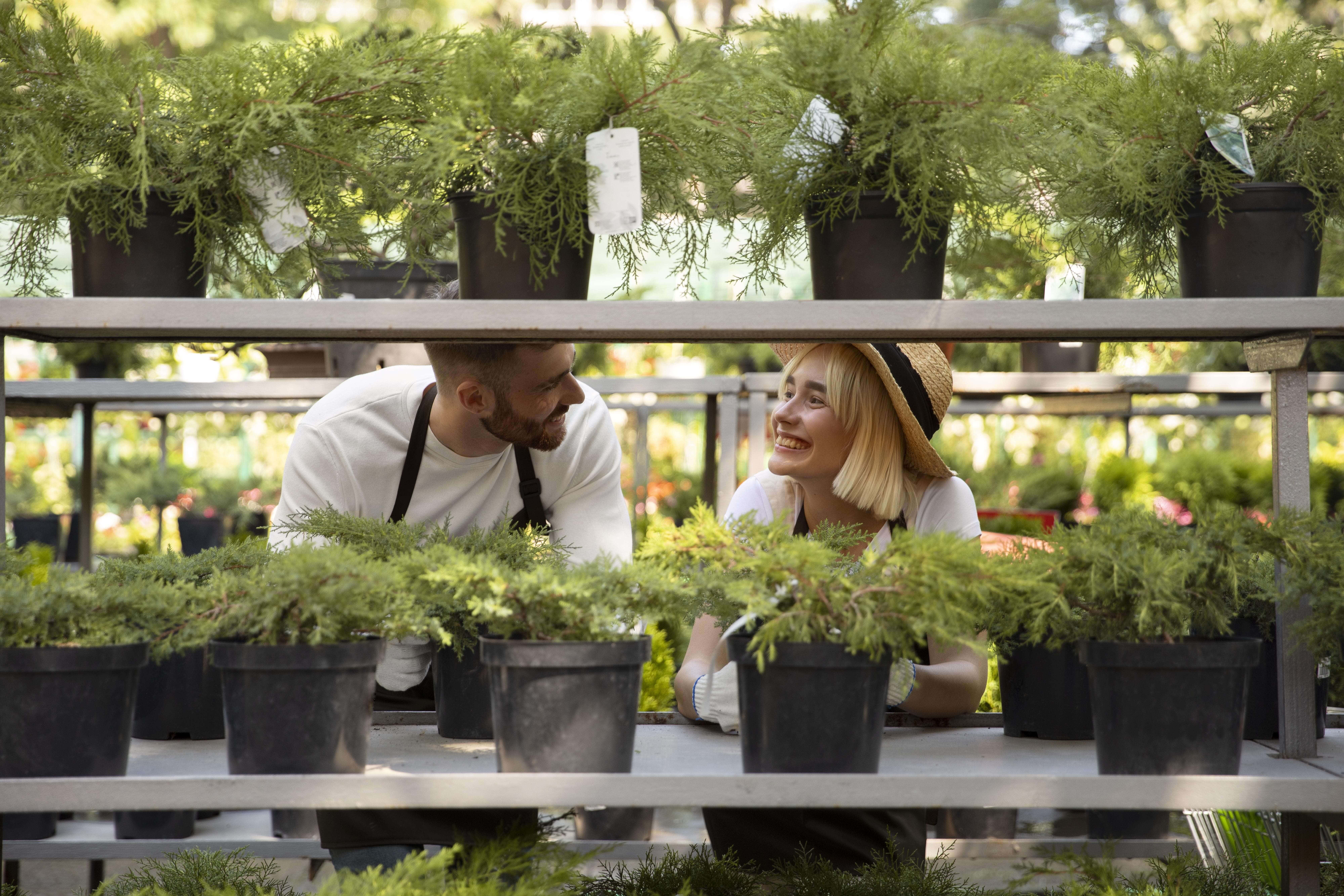 Luxury Outdoor Living Two people in aprons and gloves are smiling and talking while tending potted plants on metal shelves, creating a Luxury Outdoor Living vibe in an inviting garden center. Toronto Contractors