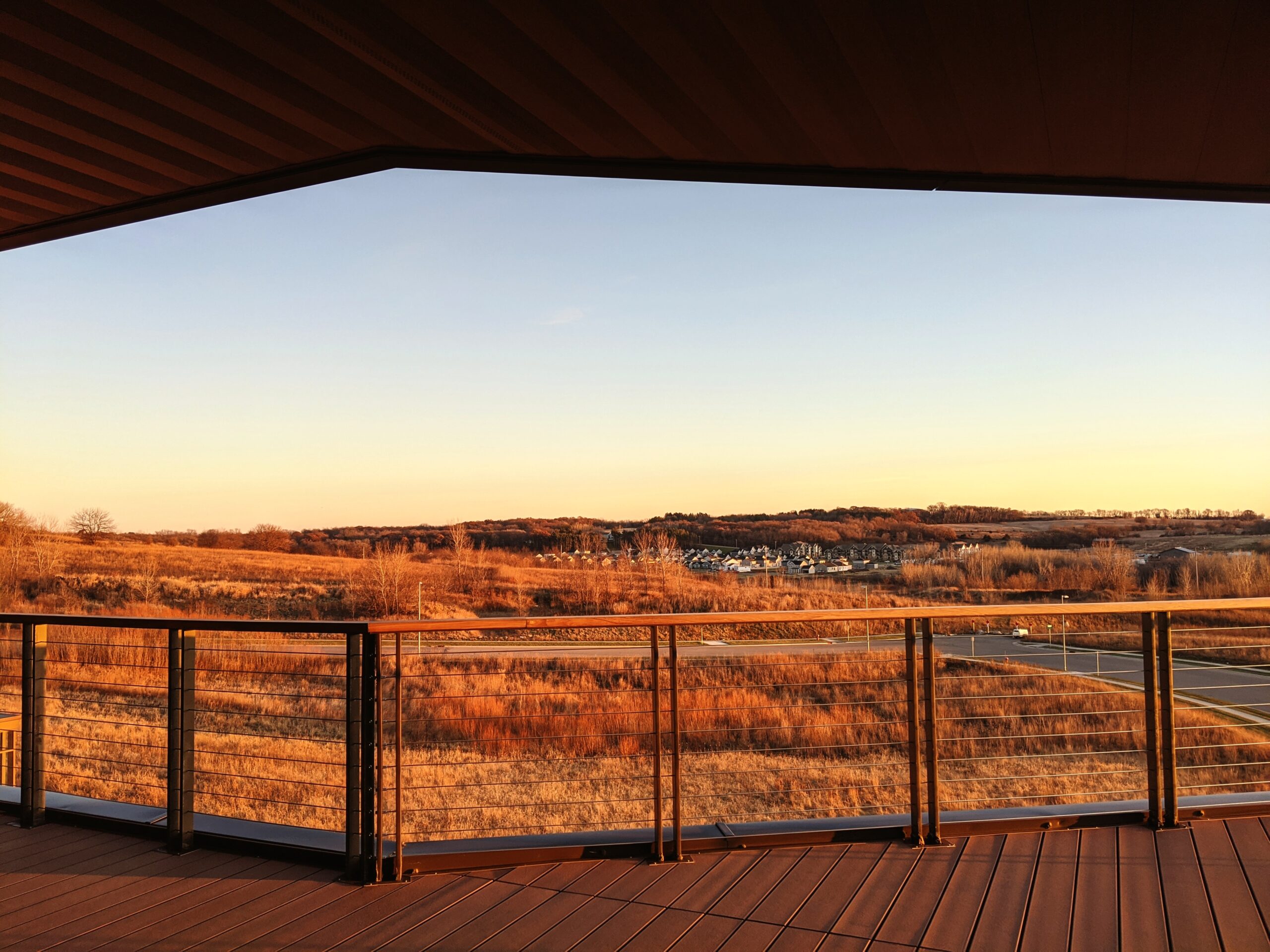 Luxury Outdoor Living Enjoy luxury outdoor living from a covered deck with a sleek metal railing, overlooking sunlit grassy hills and distant houses beneath a clear sky. Toronto Contractors