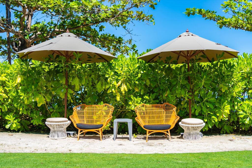 Luxury Outdoor Living Experience luxury outdoor living with two pairs of wicker chairs and small tables arranged under large umbrellas, set in front of green bushes on a sandy outdoor area. Toronto Contractors