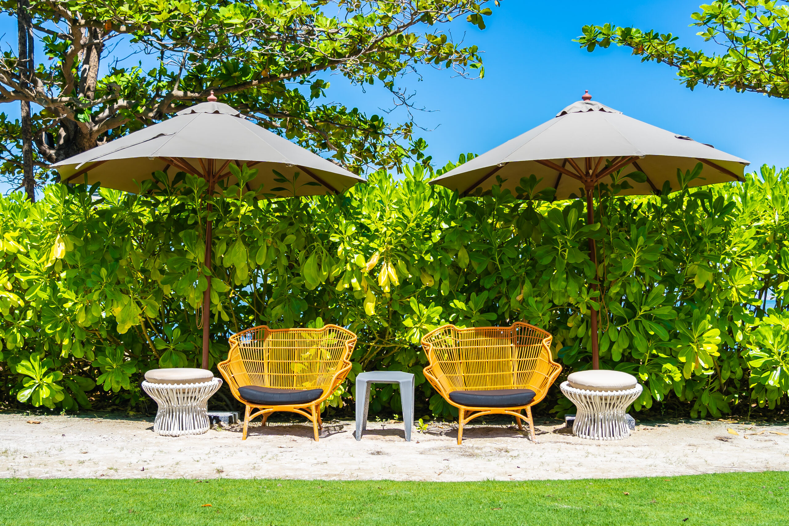 Luxury Outdoor Living Experience luxury outdoor living with two pairs of wicker chairs and small tables arranged under large umbrellas, set in front of green bushes on a sandy outdoor area. Toronto Contractors