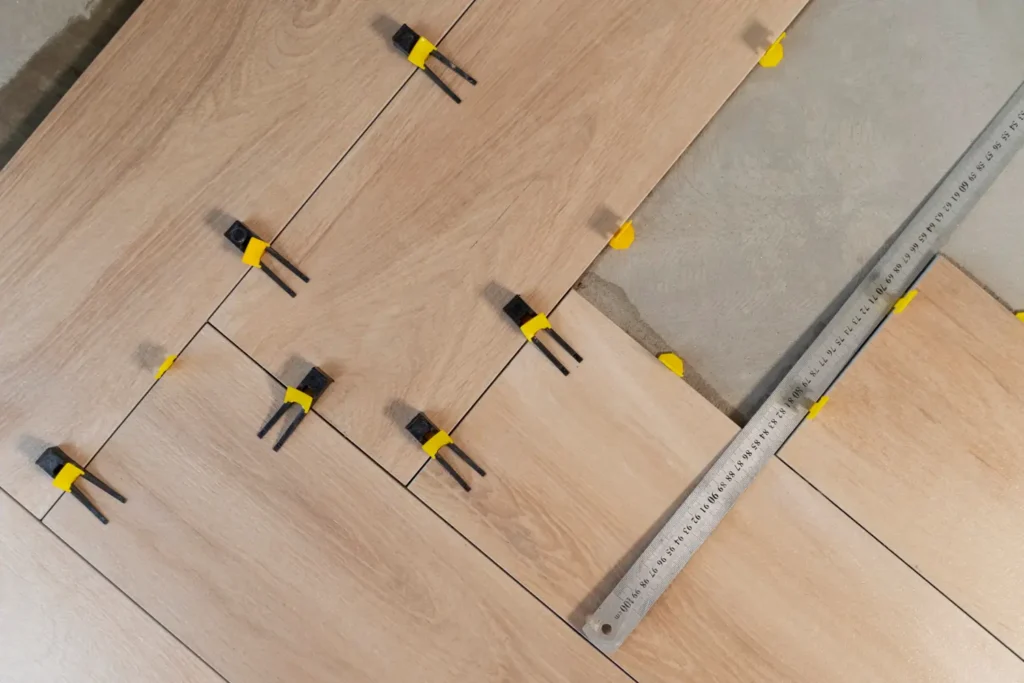 Luxury Outdoor Living Wood-look floor tiles are being installed with yellow leveling spacers and a metal ruler placed on the right side on a cement surface. Toronto Contractors