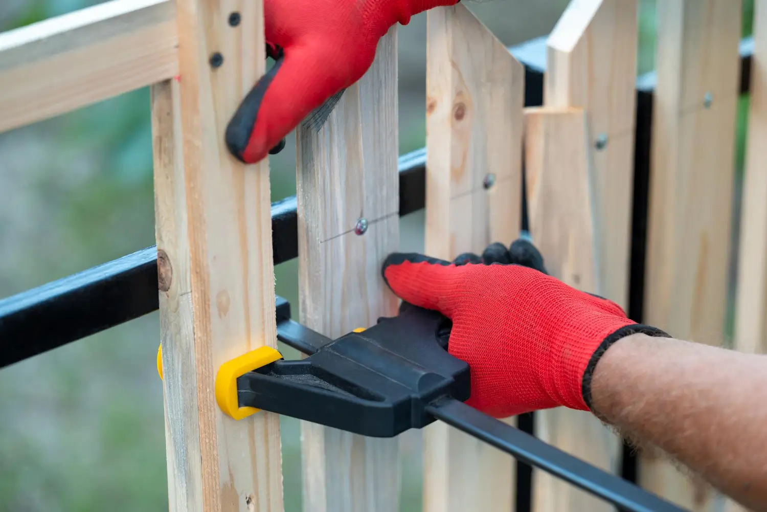 Luxury Outdoor Living A person wearing red gloves uses a clamp to hold wooden planks together for assembly or construction. Toronto Contractors
