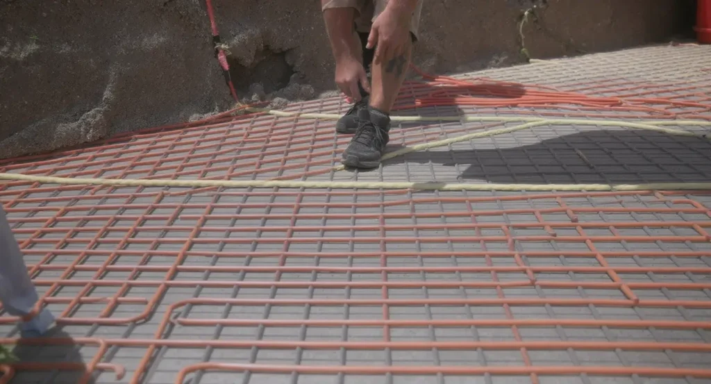 Luxury Outdoor Living A person bends down on a construction site, working on a grid of steel rebar and orange tubing laid out for a concrete foundation. Toronto Contractors