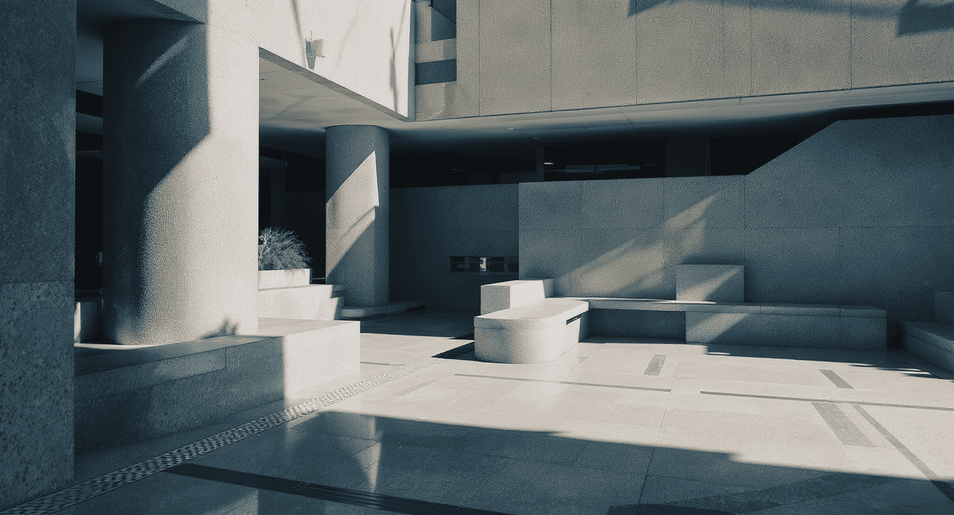 Luxury Outdoor Living Modern concrete courtyard with geometric benches, large pillars, and angular shadows cast by sunlight, creating a structured, minimalist architectural scene. Toronto Contractors